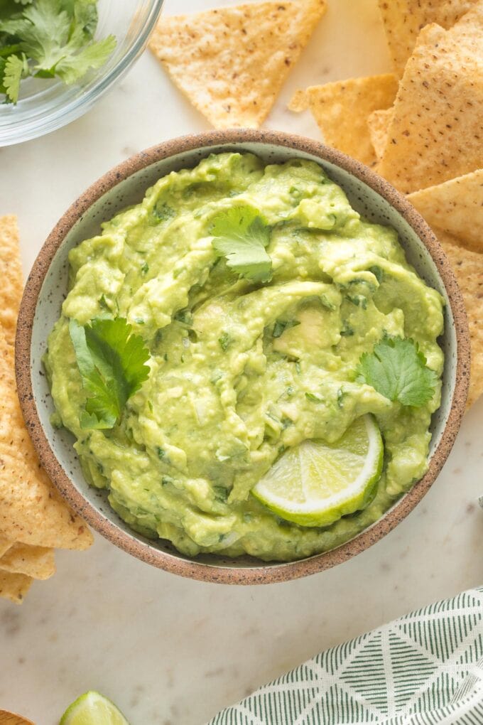 Small bowl of guacamole garnished with lime wedges and cilantro.