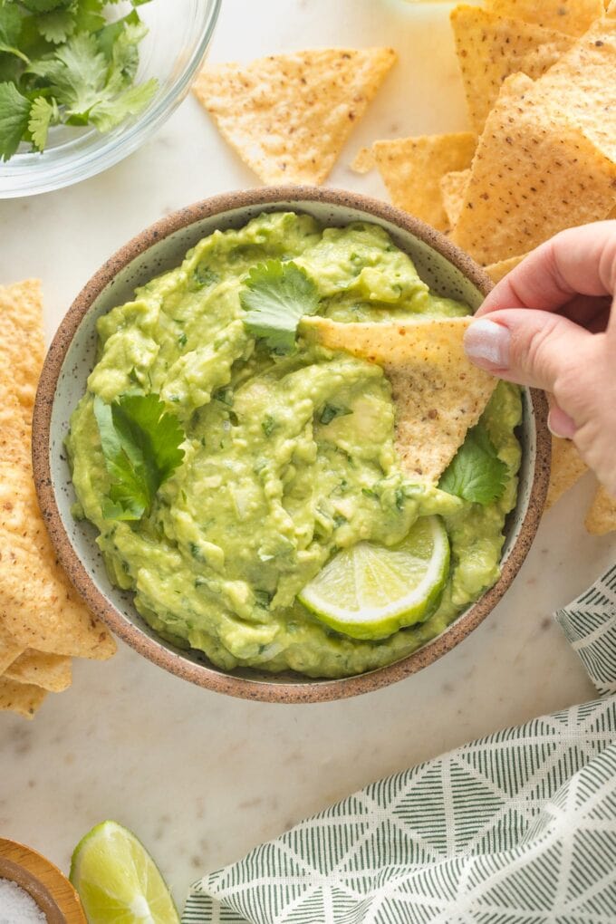 Hand dipping a crisp tortilla chip into a bowl of homemade guacamole.