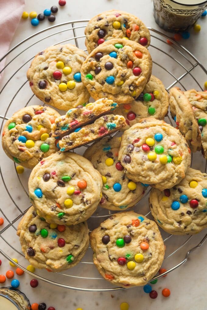 Cooling rack full of chocolate chip M&M cookies with a nearby glass of milk.