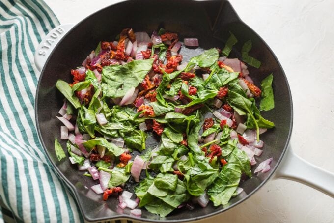 Spinach, onion, and sun-dried tomato sauteed in a skillet.