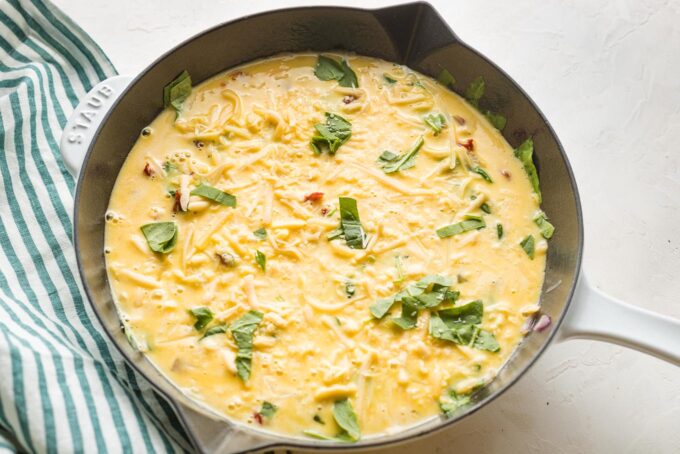 Eggs poured into skillet on top of veggies and cheese.