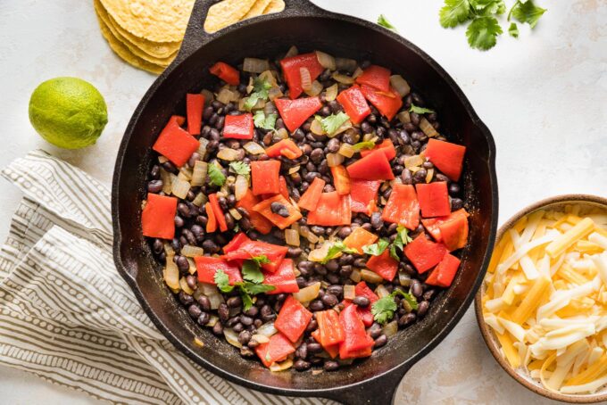 Cast iron skillet filled with a mixture of cooked seasoned black beans and roasted red peppers.