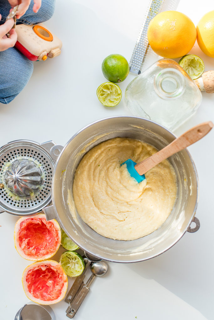 Paloma cupcake batter in a mixing bowl surrounded by fresh-squeezed grapefruit and lime.