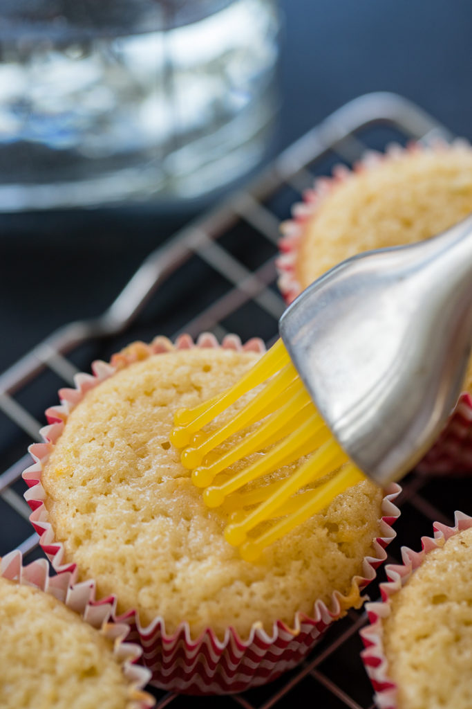 Using a pastry brush to brush tequila onto the tops of baked Paloma cupcakes.