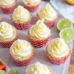 Paloma cupcakes frosted and lined up, with grapefruit and lime wedges and a bottle of tequila in the background.