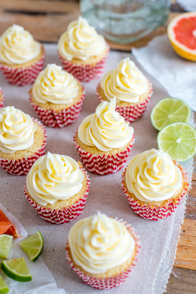 Paloma cupcakes frosted and lined up, with grapefruit and lime wedges and a bottle of tequila in the background.