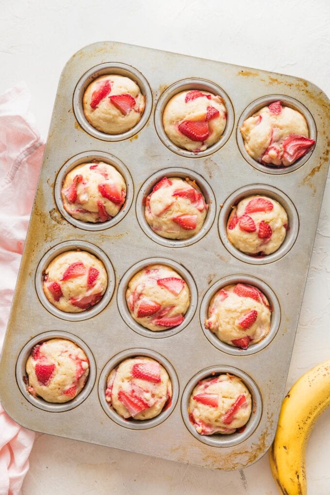 Muffin pan filled with 12 strawberry banana muffins, fresh out of the oven.