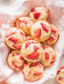 Close up of strawberry banana muffins heaped in a basket lined with a pink kitchen towel.