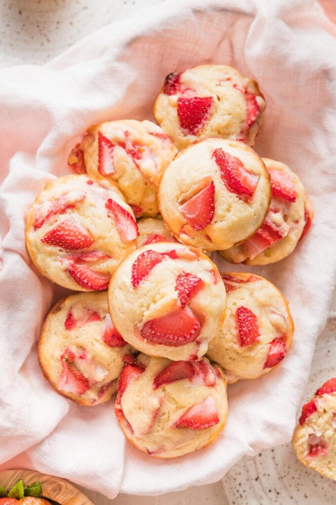 Close up of strawberry banana muffins heaped in a basket lined with a pink kitchen towel.