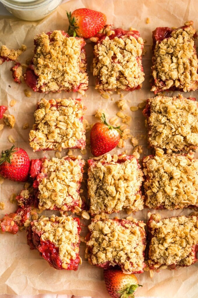 Overhead image of strawberry rhubarb crumble bars, cut into squares and spread out on parchment.