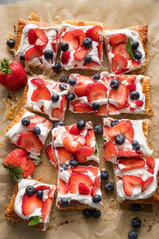 Sliced tart made of puff pastry topped with whipped mascarpone cheese and fresh strawberries and blueberries.