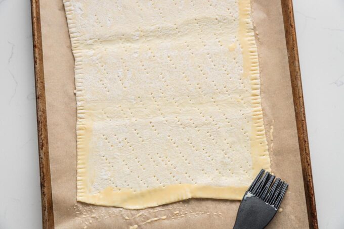 Puff pastry rectangle placed on a parchment-lined baking sheet and brushed with an egg wash on the outer rim.