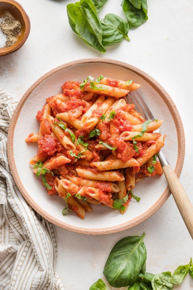 Small shallow bowl filled with a serving of pasta marinara garnished with slivers of fresh basil.