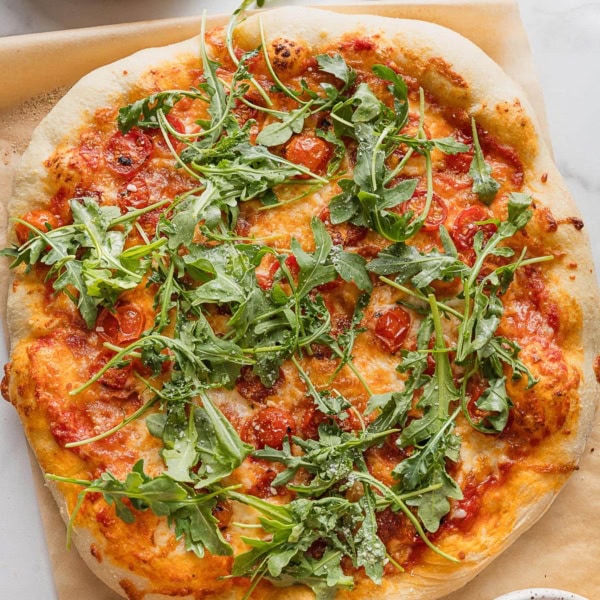 Homemade pizza with roasted cherry tomatoes, crisp crumbled bacon, and fresh arugula on top.
