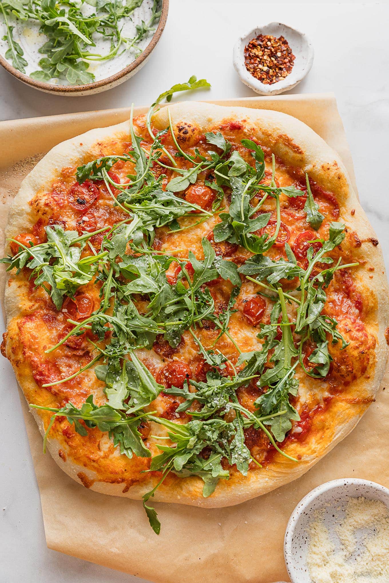 Homemade pizza with roasted cherry tomatoes, crisp crumbled bacon, and fresh arugula on top.