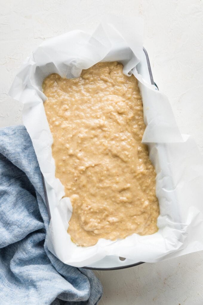 Banana bread batter spread in a 9"x5" loaf pan lined with white parchment paper and ready to bake.