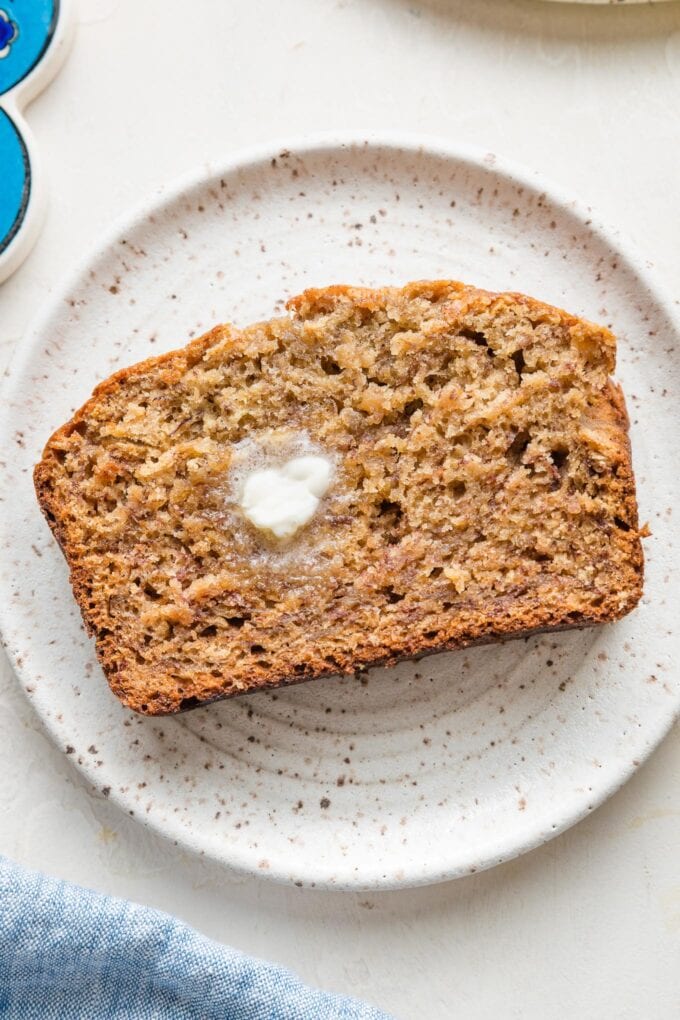 Close up overhead image of a slice of banana bread with a pat of butter melting on it.