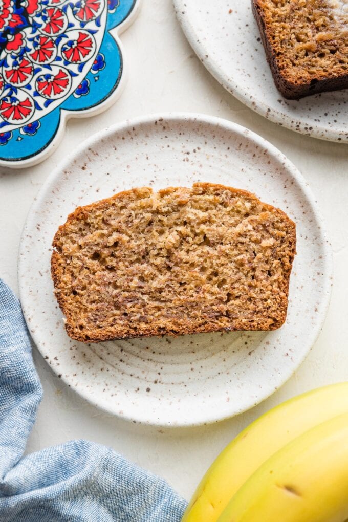 A slice of tender, moist banana bread made with five bananas on a plate about to be eaten.