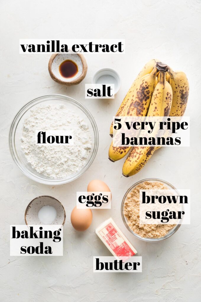 Labeled overhead photo of the ingredients for a banana bread loaf using five bananas: all-purpose flour, 5 very ripe bananas, vanilla extract, salt, baking soda, butter, eggs, and brown sugar.