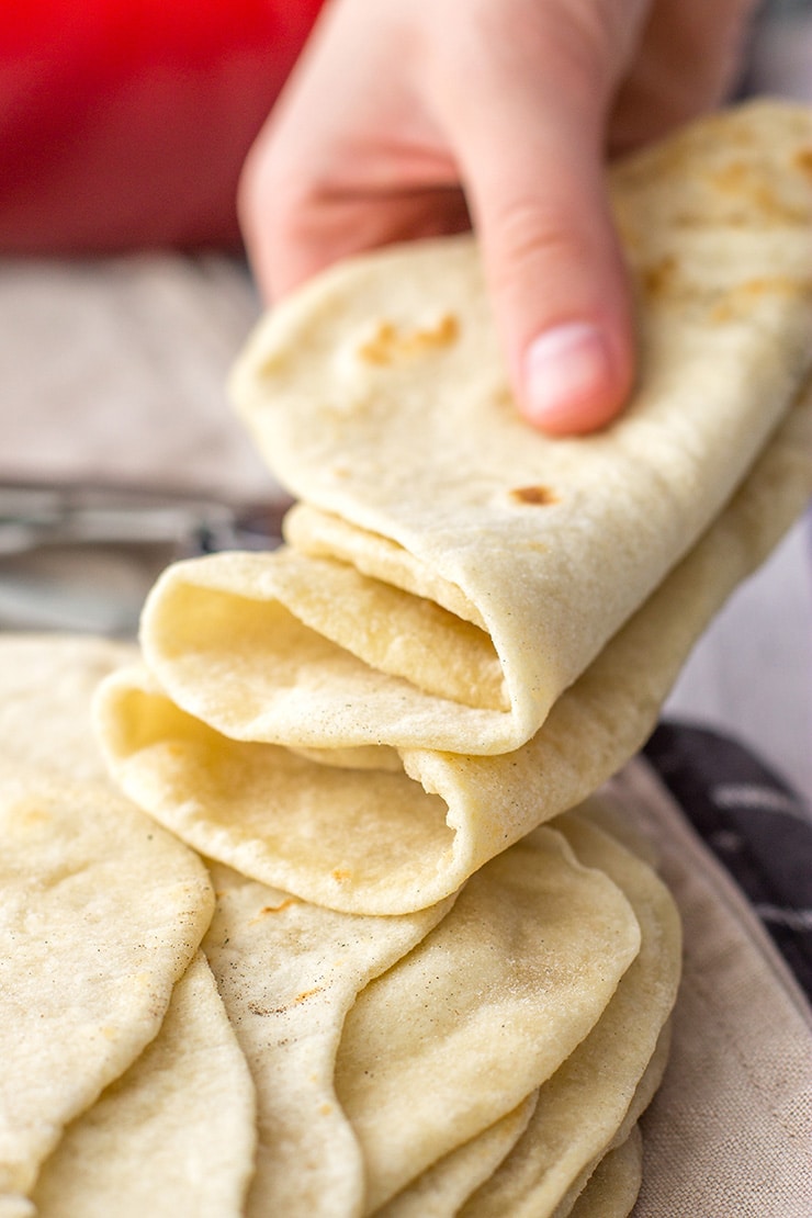 A hand holding a stack of soft, pliable homemade flour tortillas.