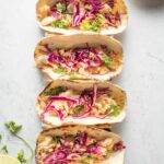 Four jalapeno lime fish tacos with shredded cabbage, lined up in a row.