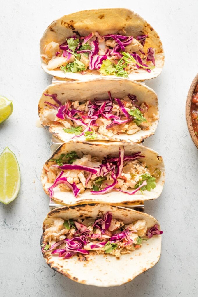 Four jalapeno lime fish tacos with shredded cabbage, lined up in a row.