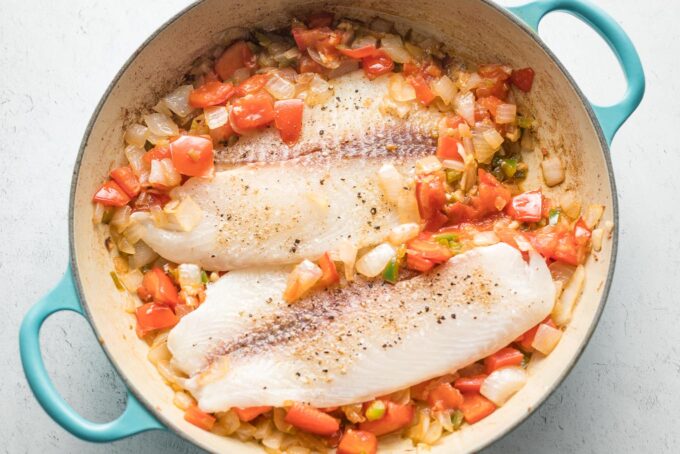 Raw fish fillets added to skillet.