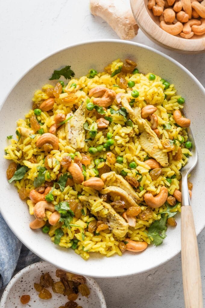 Low bowl filled with a helping of curry cashew chicken and rice with peas and cilantro.