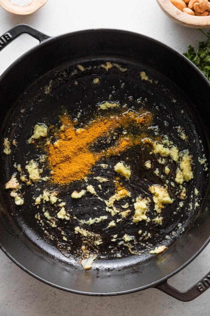 Curry powder and fresh grated ginger being fried in a deep cast iron skillet.