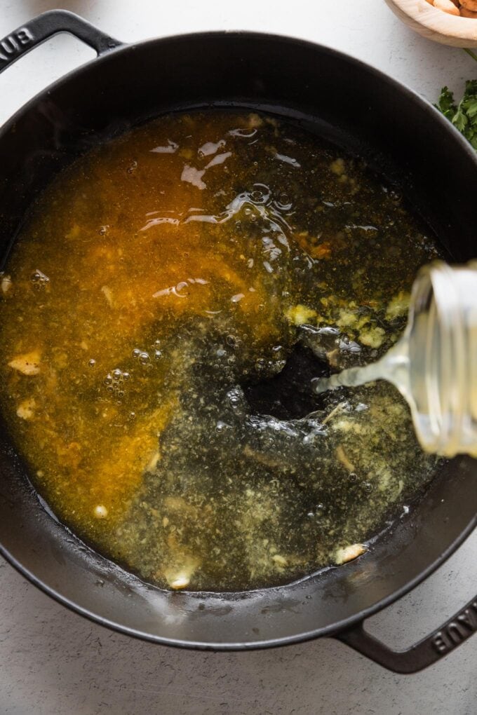 Broth being poured from a jar into a skillet with curry powder and ginger.