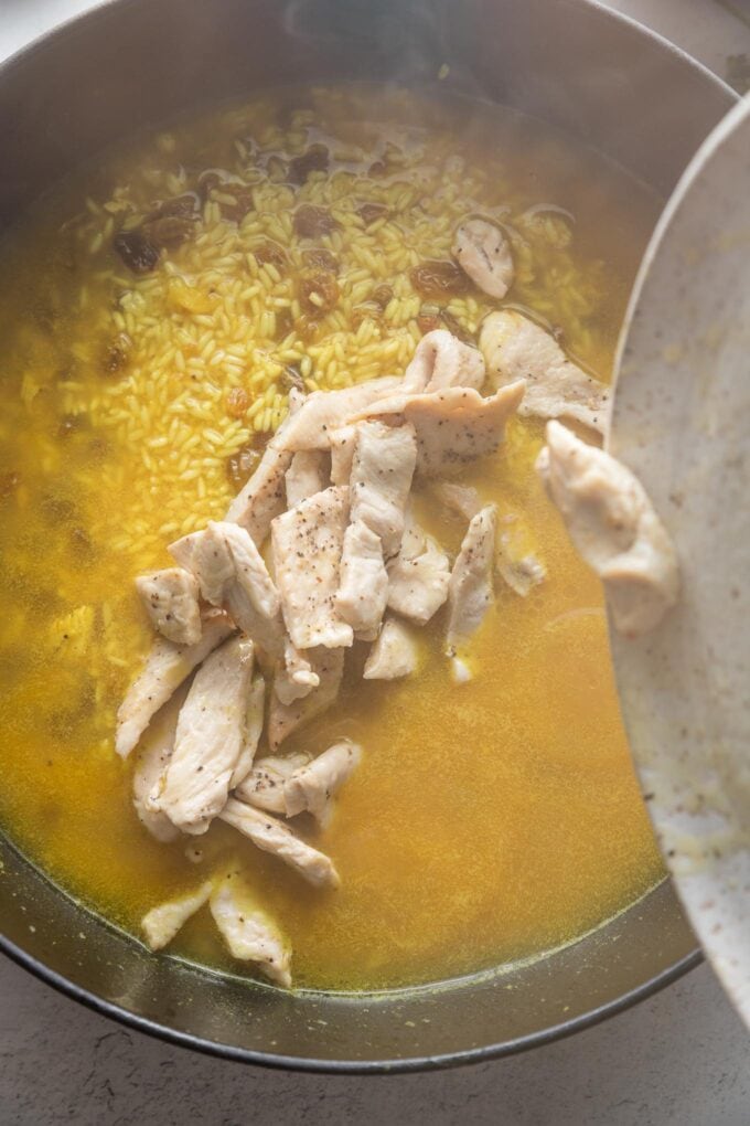 Chicken pieces being transferred back into a cast iron skillet with broth and rice.