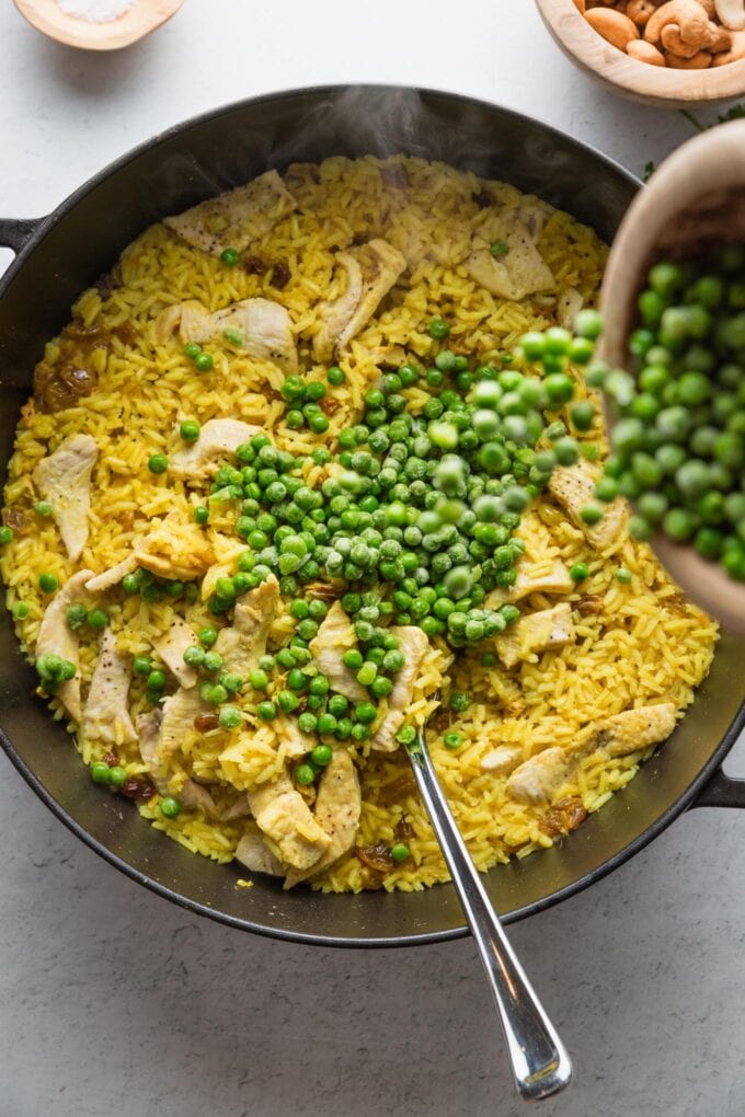 Peas being poured into a one pot curry rice dish.