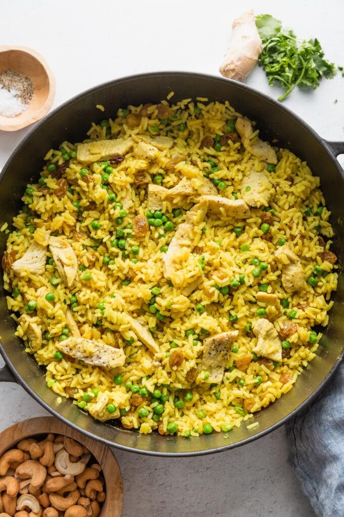 Peas stirred into a cast iron pot with chicken and curry spiced rice.