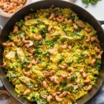 Large cast iron skillet filled with a one pot meal of curry spiced chicken with cashews, rice, and peas.