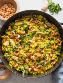 Large cast iron skillet filled with a one pot meal of curry spiced chicken with cashews, rice, and peas.