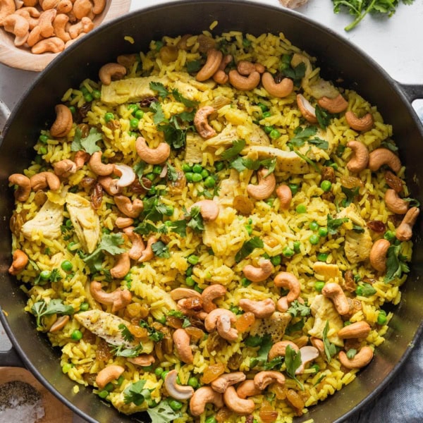Large cast iron skillet filled with a one pot meal of curry spiced chicken with cashews, rice, and peas.