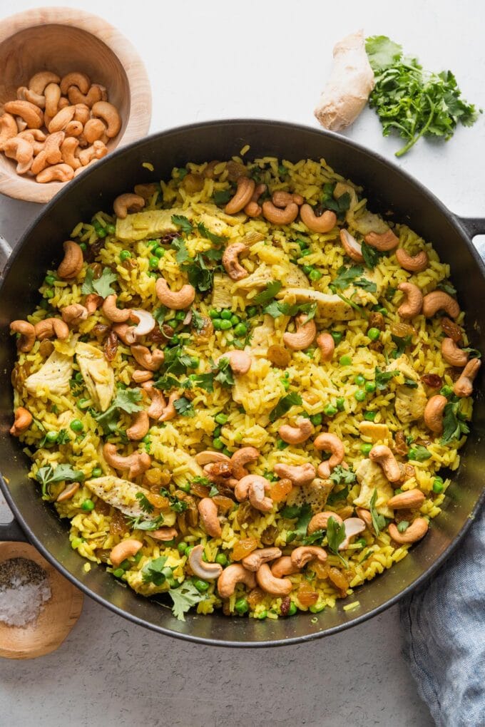 Large cast iron skillet filled with a one pot meal of curry spiced chicken with cashews, rice, and peas.