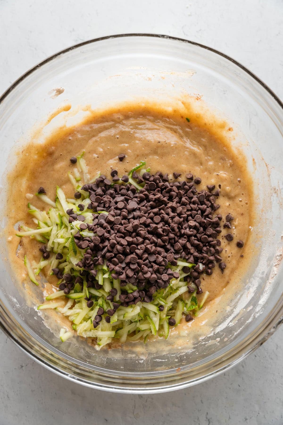Shredded zucchini and mini chocolate chips sprinkled over muffin batter.