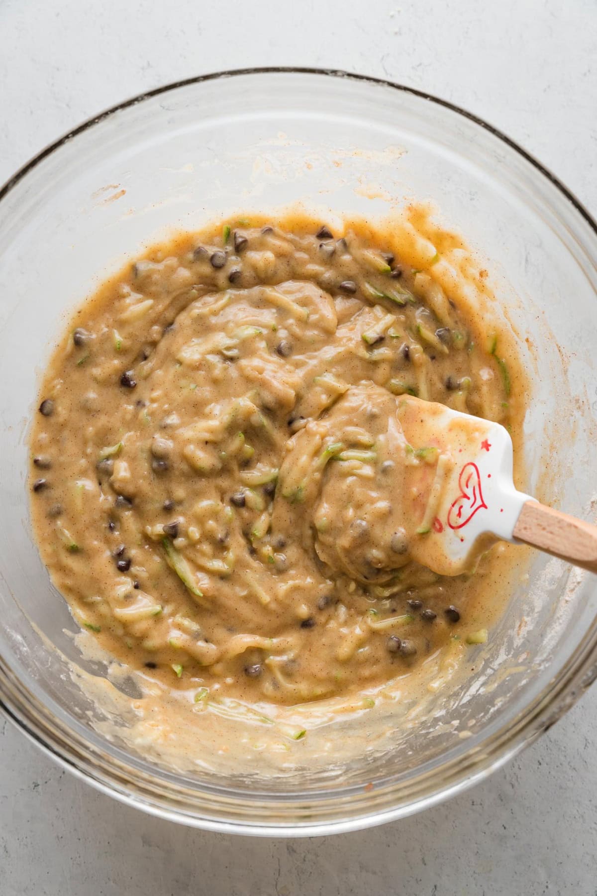Spatula folding together a batter for chocolate chip zucchini muffins.