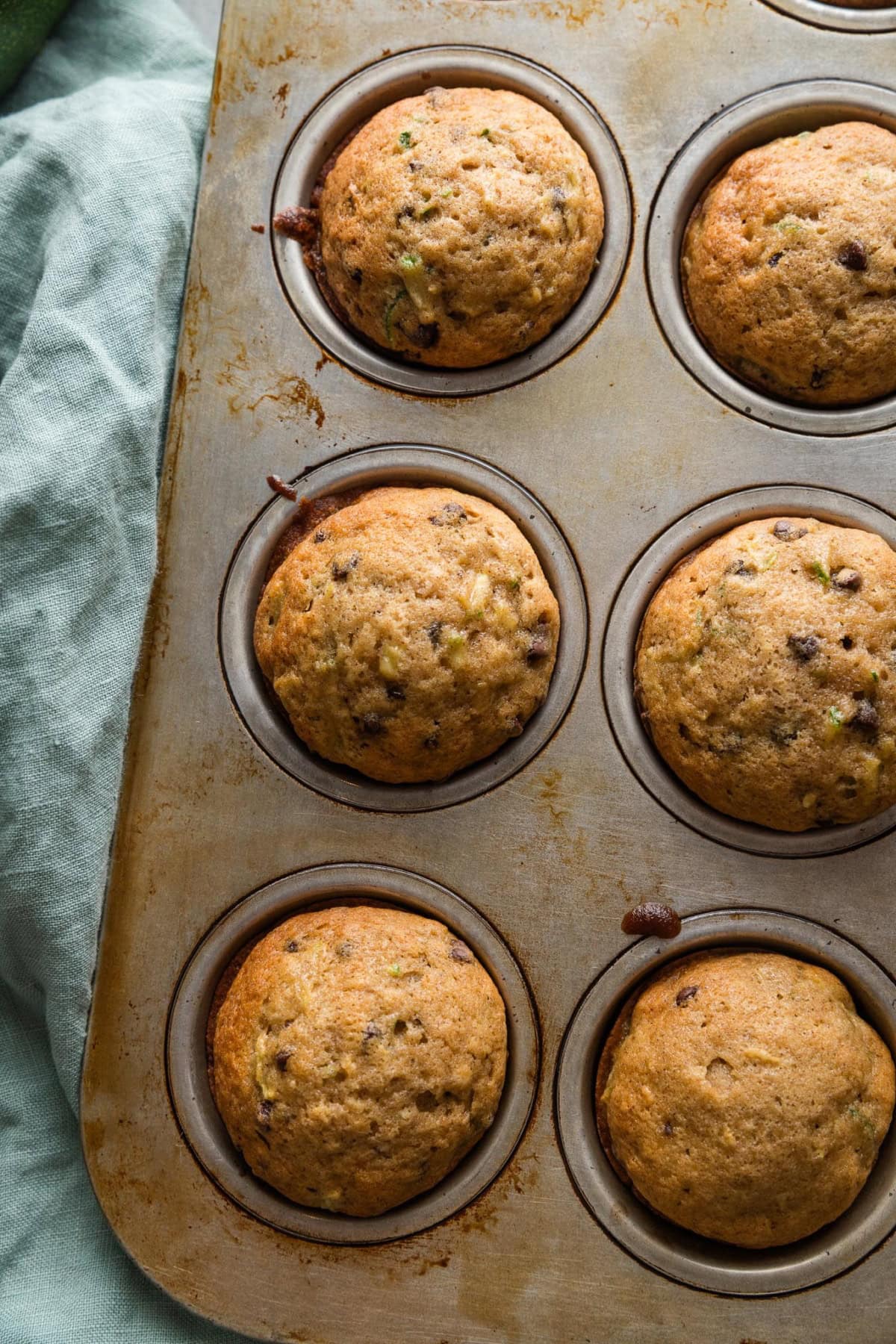 Close up of nicely domed zucchini muffins cooling inside a metal muffin tray.