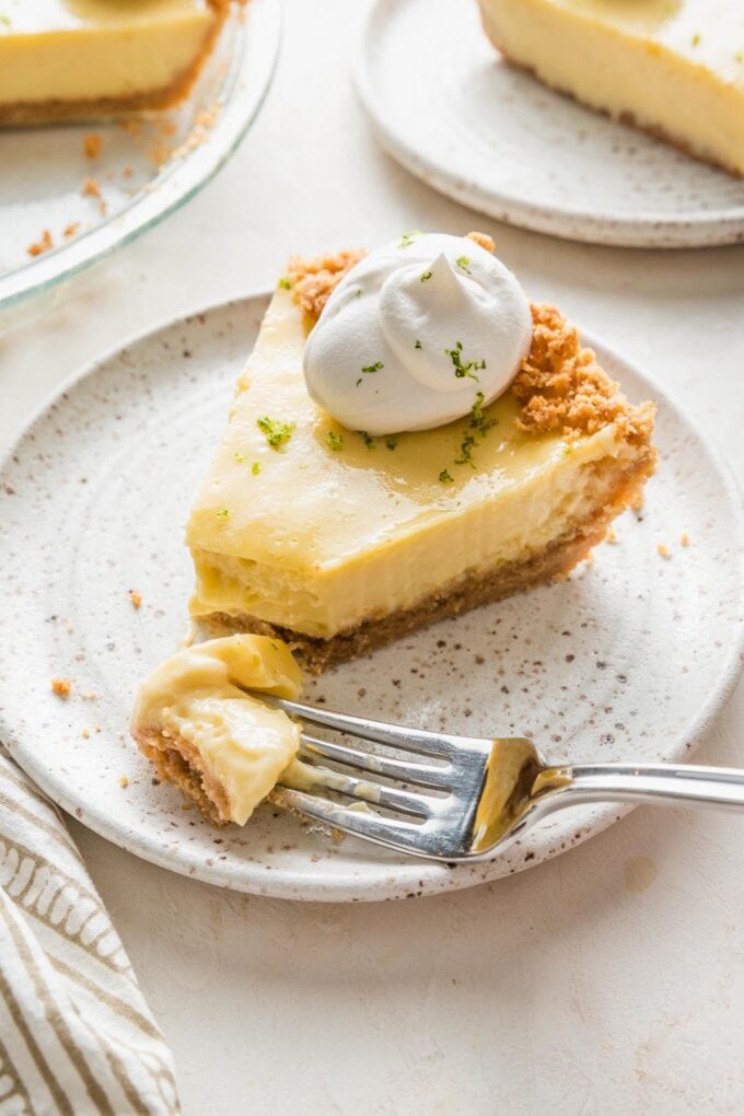 Close up of a forkful of key lime pie speared off and set on a small white plate.