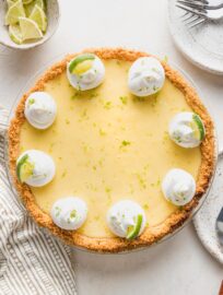 Overhead image of a whole key lime pie garnished with whipped cream, lime slices, and lime zest.