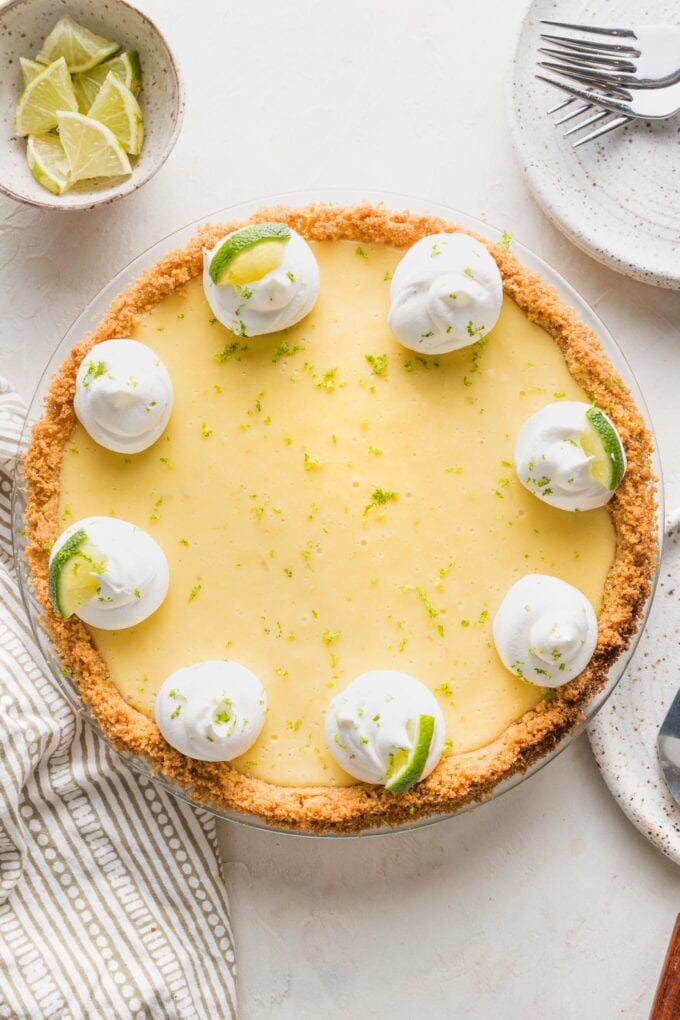 Overhead image of a whole key lime pie garnished with whipped cream, lime slices, and lime zest.
