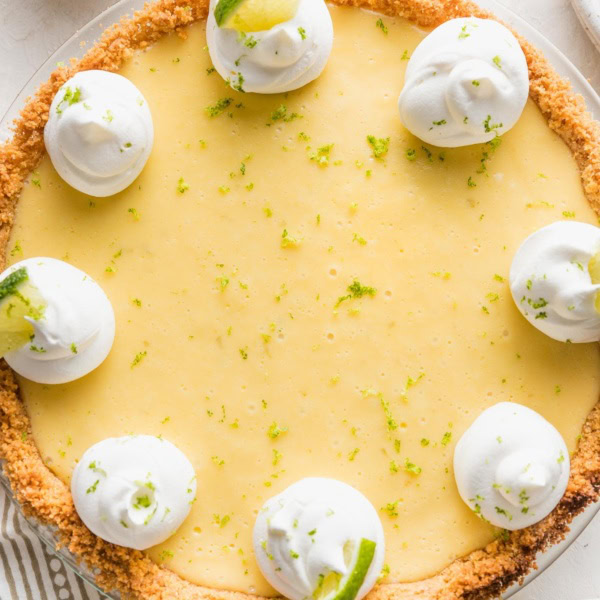 Overhead image of a whole key lime pie garnished with whipped cream, lime slices, and lime zest.