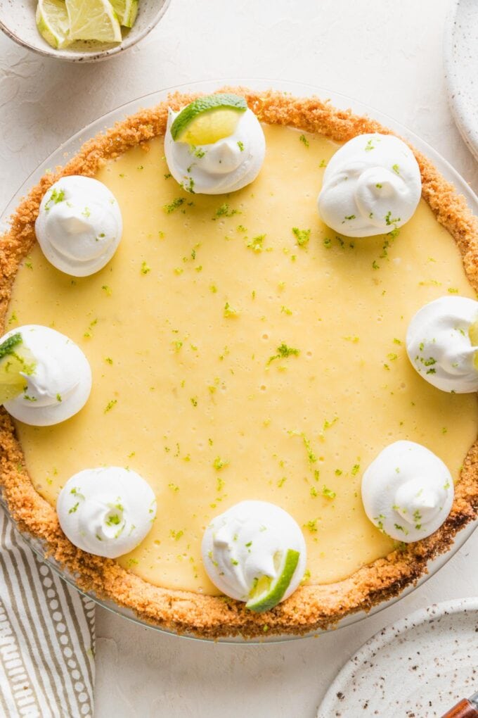 Overhead image of a whole key lime pie garnished with whipped cream, lime slices, and lime zest.