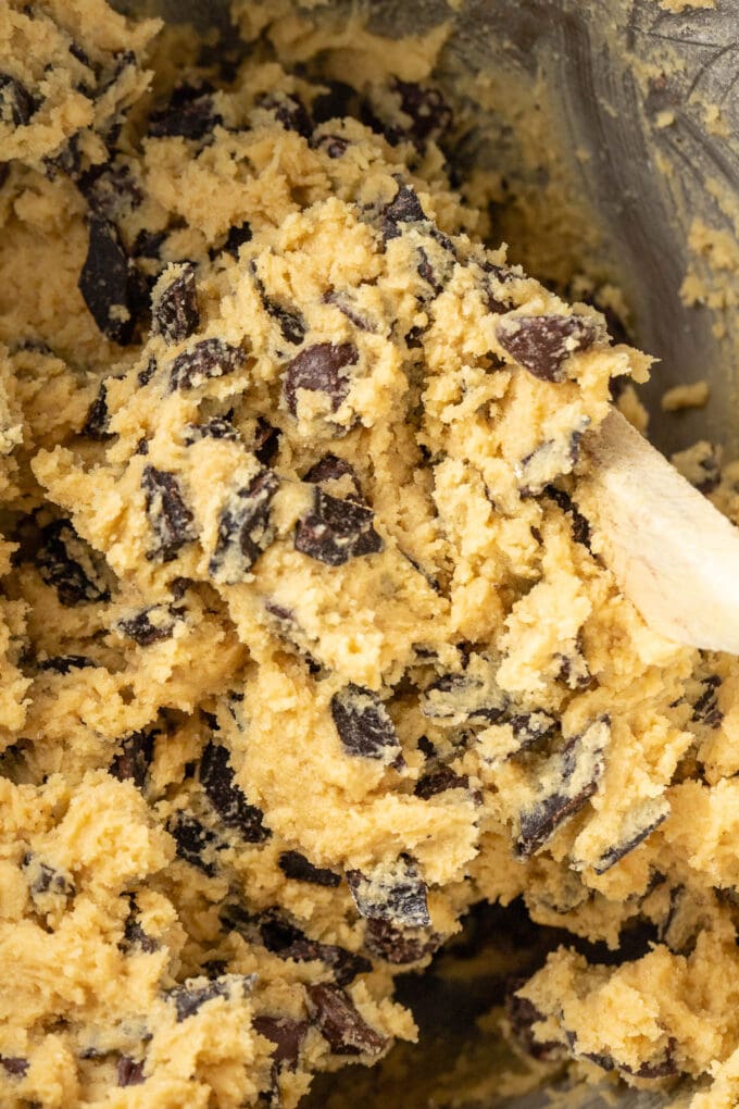 Close-up of chocolate chip cookie dough being mixed with a wooden spoon.