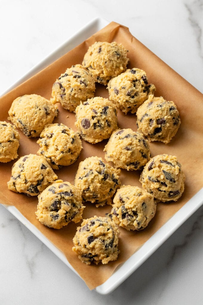 Balls of chocolate chip cookie dough on a parchment paper-lined plate, ready to be flash frozen.