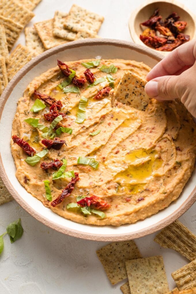 Hand dipping a cracker into a bowl of dip.