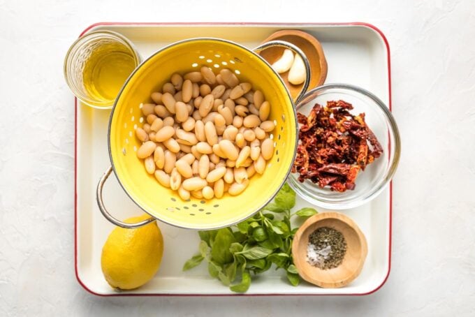 Prep bowls with ingredients: white beans, sun-dried tomatoes, basil, thyme, garlic, olive oil, salt, and pepper.