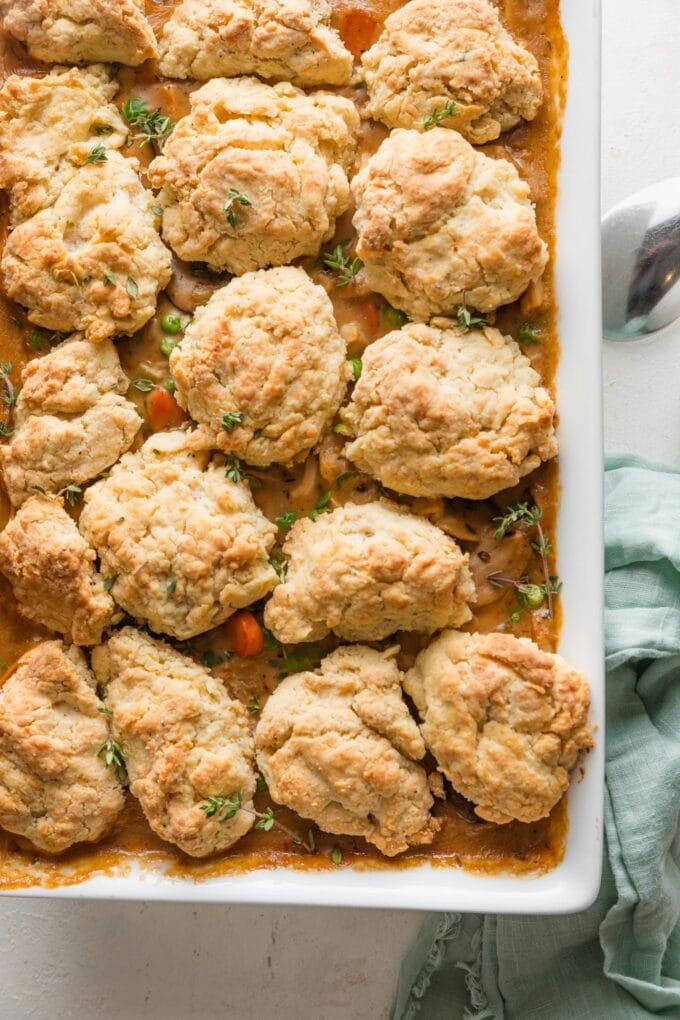 Overhead view of a chicken pot pie with biscuit crumble topping in a white ceramic baking dish, just pulled from the oven and cooling on the counter.